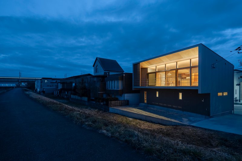 Two-story residence with illuminated glass facade overlooking neighboring houses at dusk