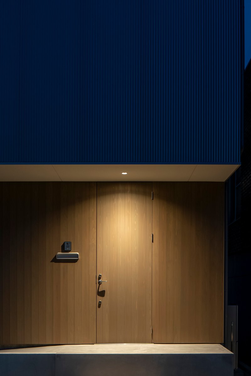Recessed entry with vertical timber door and mailbox under a dark corrugated metal soffit