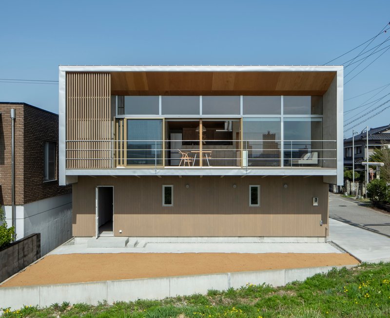 Street view showing the two-story facade with vertical timber slats, glazed upper level terrace, and beige concrete base