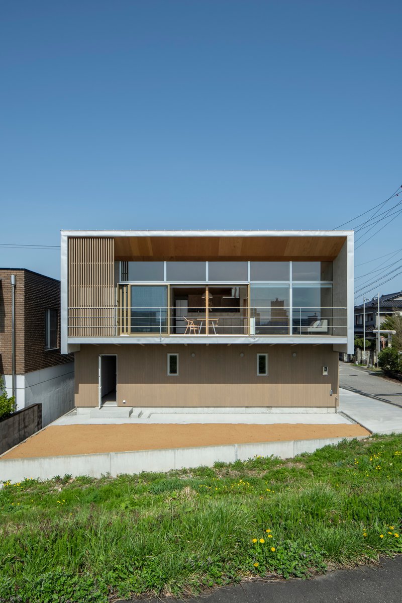 Front elevation with upper level timber screening, glass balustrade, and grassy foreground under clear sky