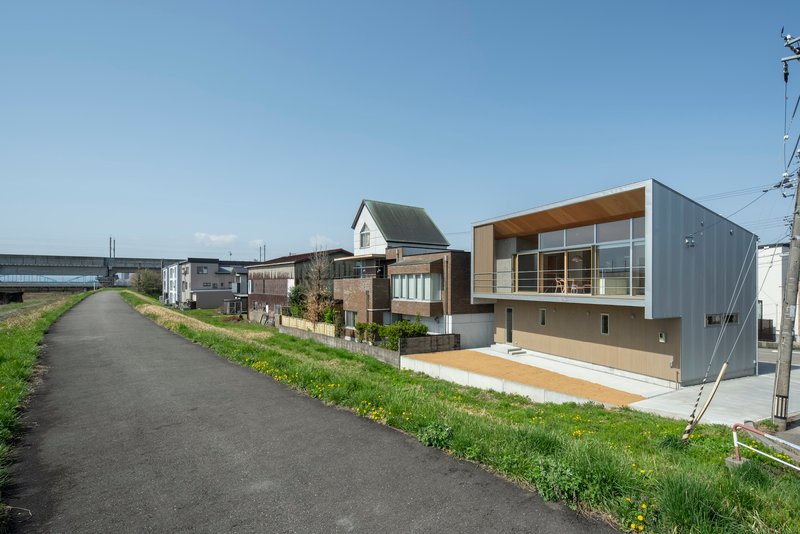 Diagonal view from adjacent path showing the house amid neighboring buildings and grassy embankment