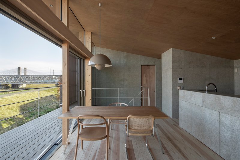 Dining area with timber table, pendant light, and concrete kitchen island overlooking the terrace