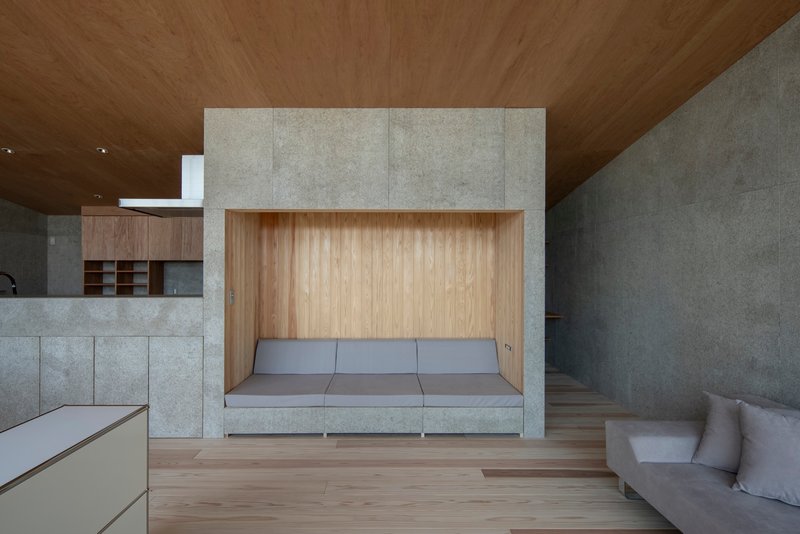 Interior living space with built-in timber bench niche framed by concrete walls under a wood ceiling