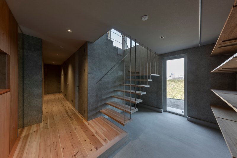Entry hall with floating timber staircase, glass railings, and grey concrete walls beside timber flooring