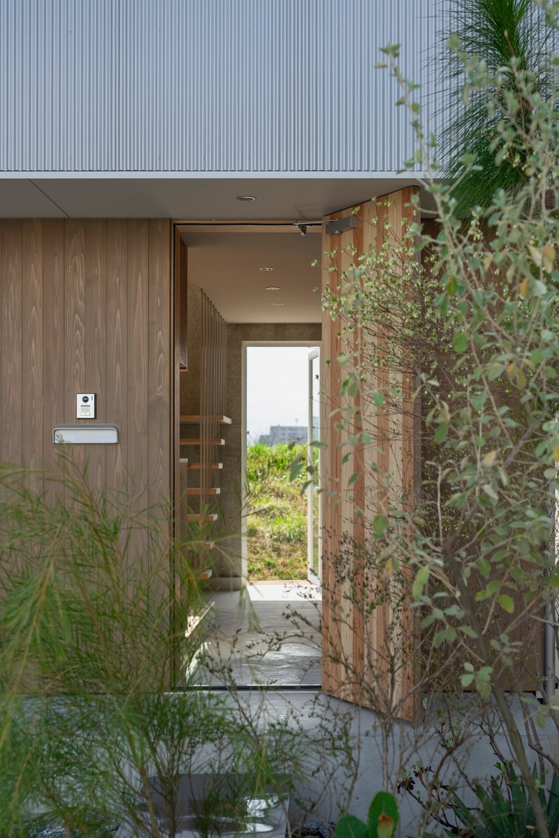 Entrance threshold framed by timber cladding and weathered steel screen with grasses in foreground