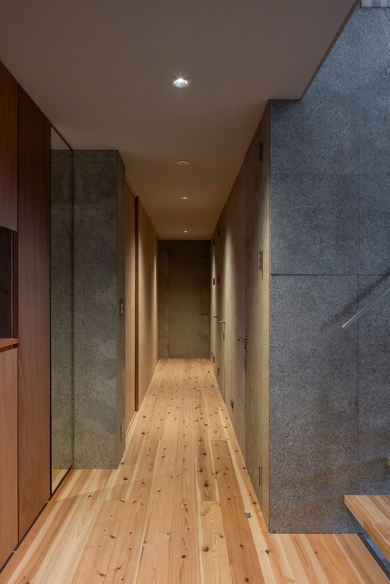 Narrow hallway with concrete walls, timber flooring, and recessed lighting along plywood ceiling