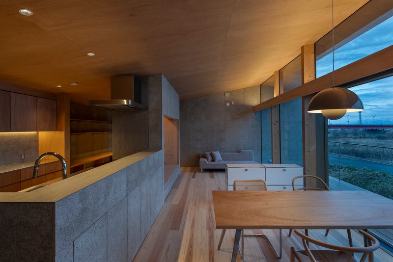 Open-plan living space with concrete kitchen island, timber dining table and clerestory windows at dusk