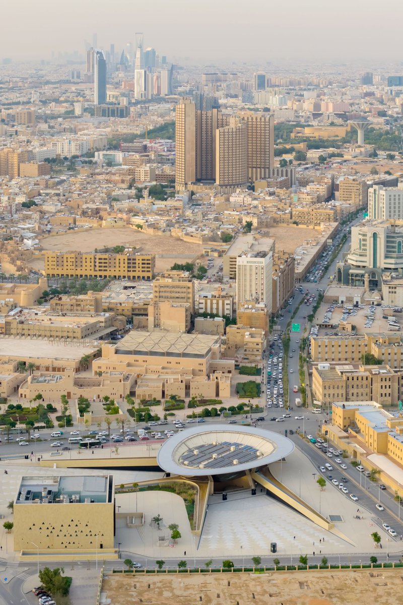 Aerial view at dusk of the circular roof puncture and curved pedestrian ramp extending toward traffic-filled streets