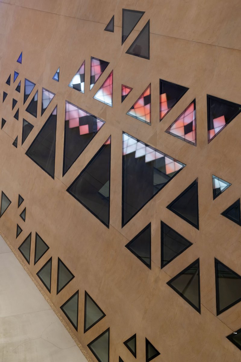 Close-up of triangular window openings in a concrete wall with colored glass reflecting interior light