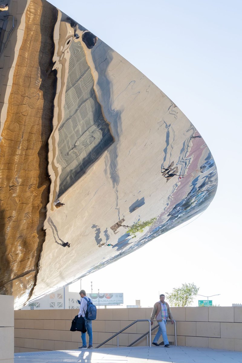 Underside view of the cantilevered canopy with bronze weathered cladding and two visitors ascending the staircase