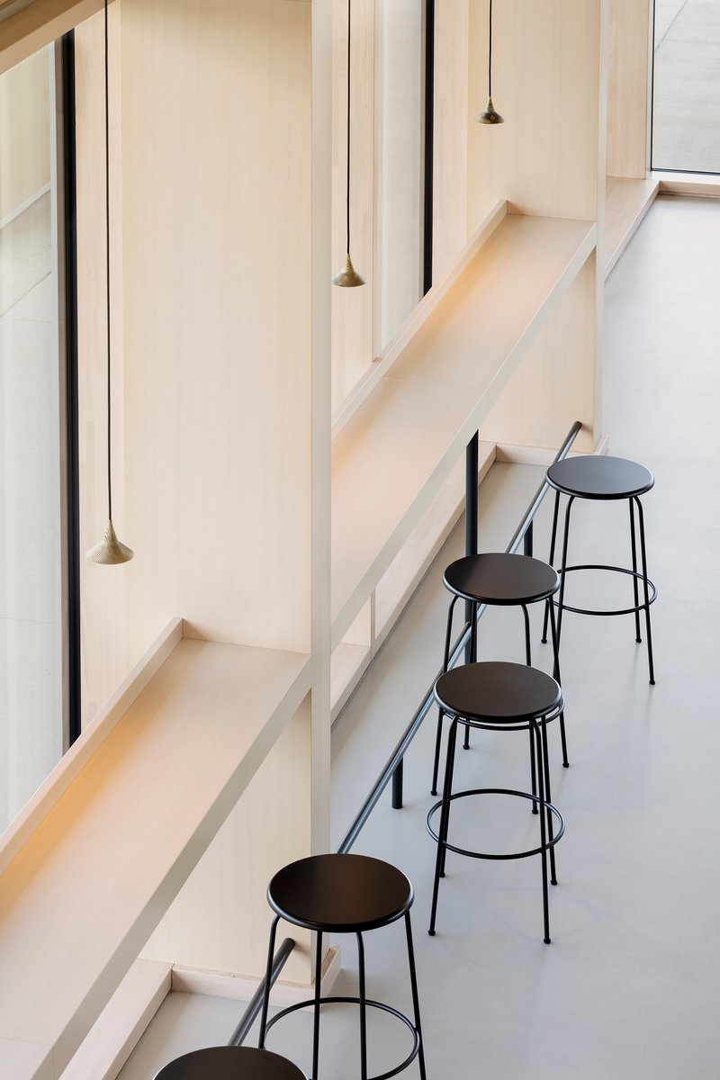 Four black metal stools beneath pale timber seating ledges and suspended conical pendant lights