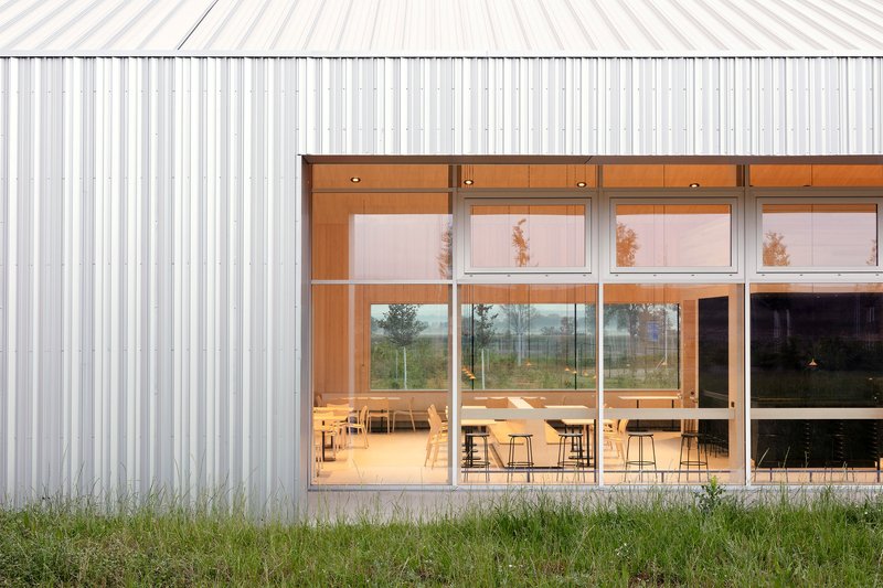 Floor-to-ceiling windows framed in timber showing interior dining tables beyond vertical metal cladding