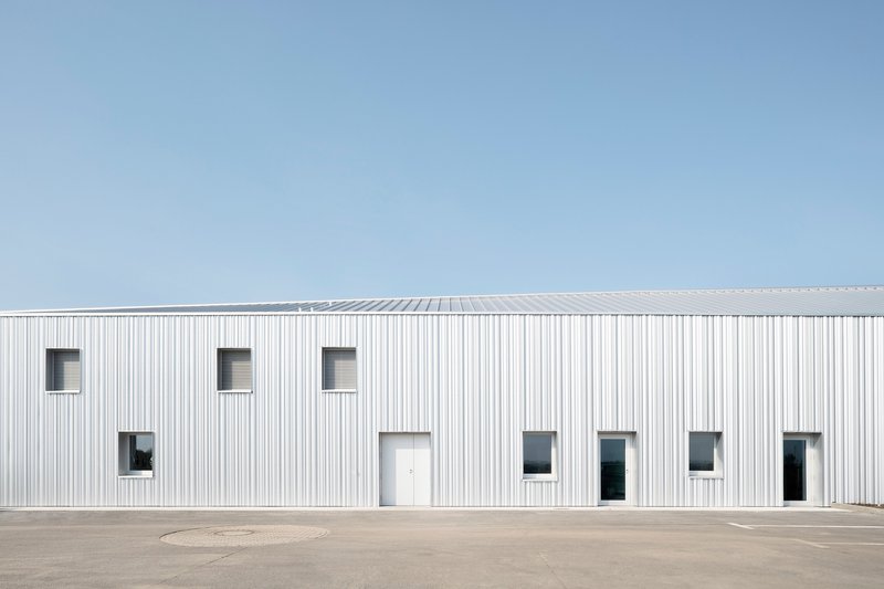 White ribbed facade with scattered rectangular window openings against a clear blue sky
