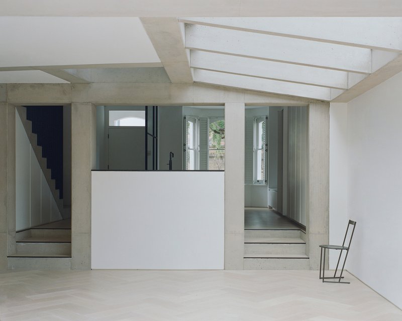 Interior room with concrete staircase and white kitchen volume beneath linear skylights
