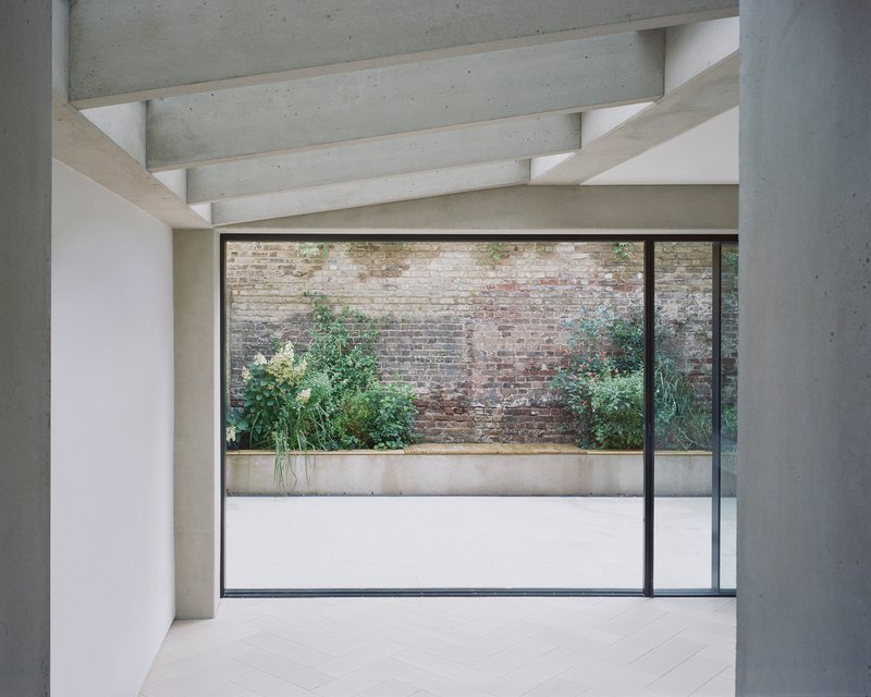 Full-height window framing courtyard with weathered brick wall and planted bed