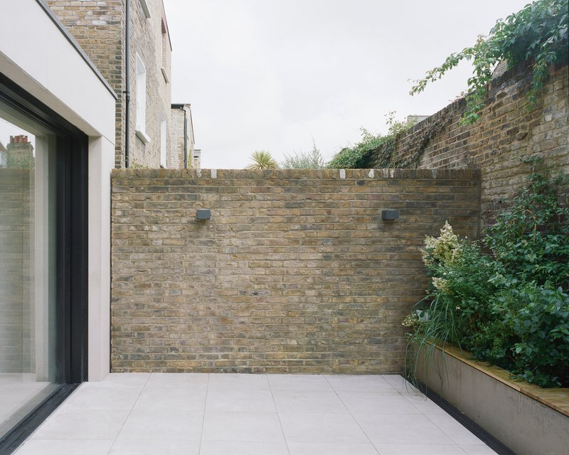 Rear courtyard terrace with buff brick walls and planted bed with greenery