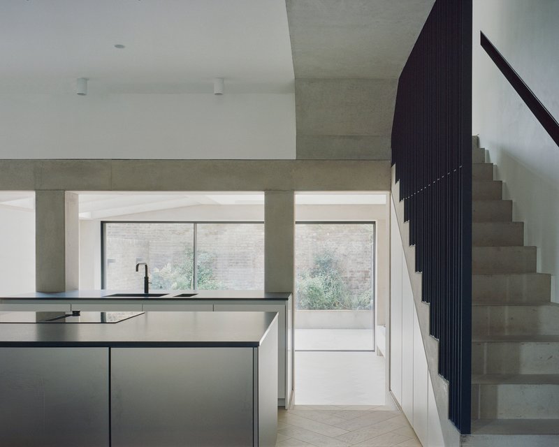 Kitchen island with dark cabinetry beneath concrete beam looking toward rear door