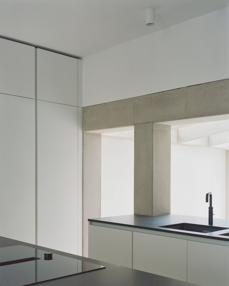 Kitchen corner showing concrete beam spanning across white cabinetry with dark countertop