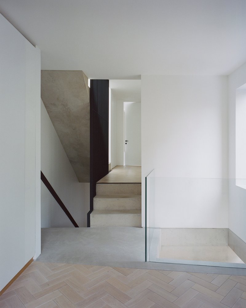 Concrete staircase with glass and metal guardrail descending to herringbone timber floor