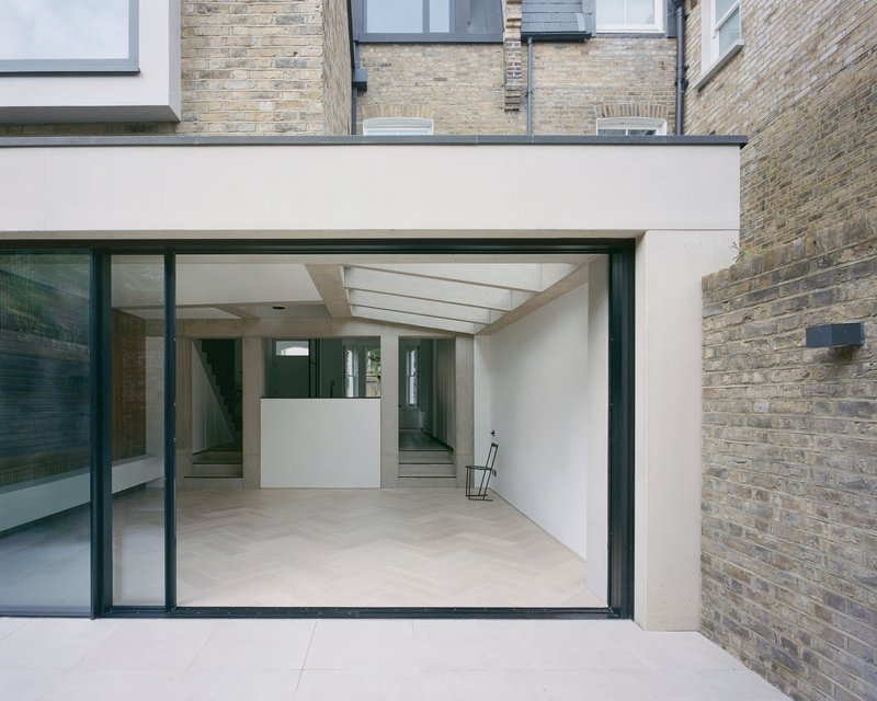Courtyard view through sliding glass doors revealing white interior volumes beneath a linear skylight