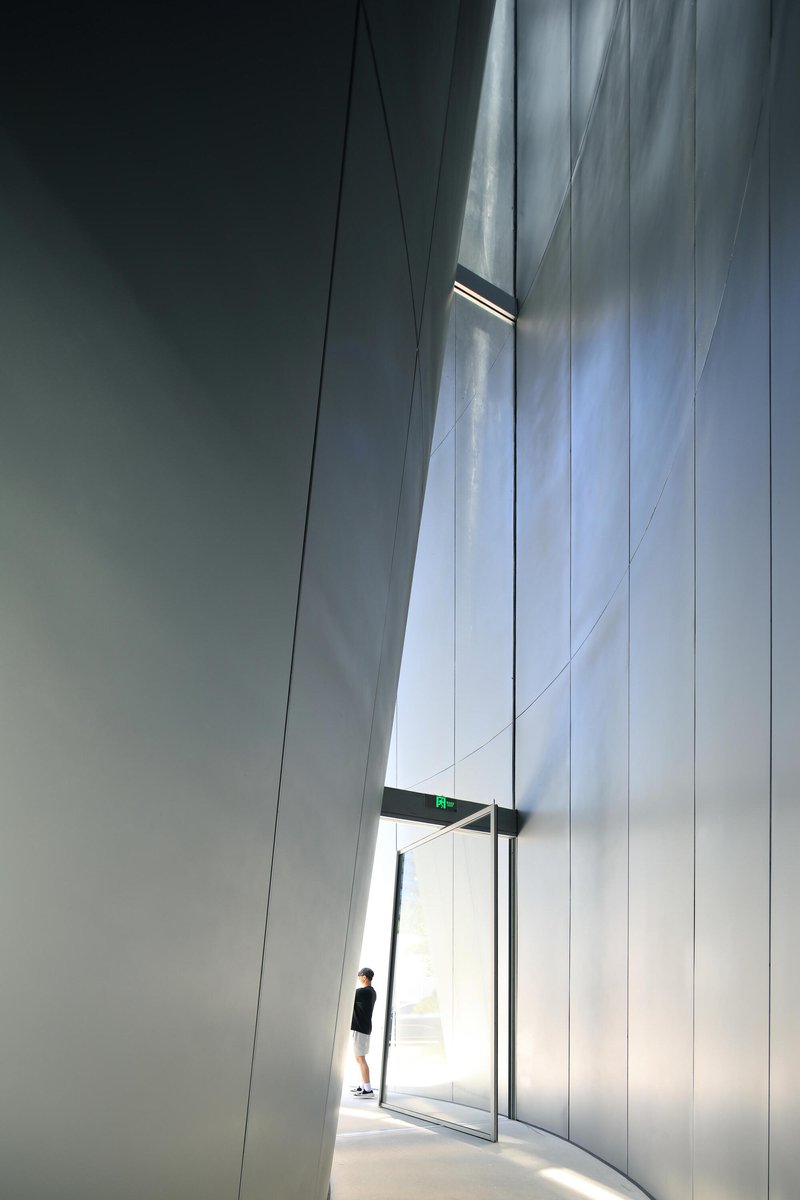 Tall lobby entrance with curved white walls and a visitor silhouetted in the backlit doorway
