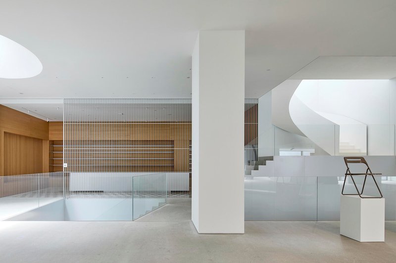 Double-height lobby space with vertical timber slat partition and curved white staircase in background