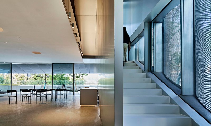 White terrazzo staircase with steel handrail ascending alongside perforated metal screen and glazed courtyard beyond