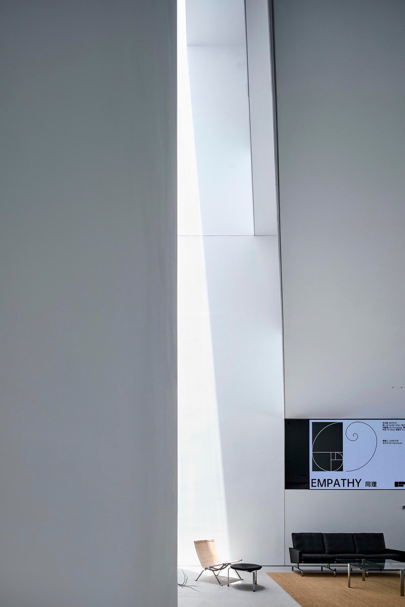 Tall vertical skylight slicing through white gallery walls with seating area visible below