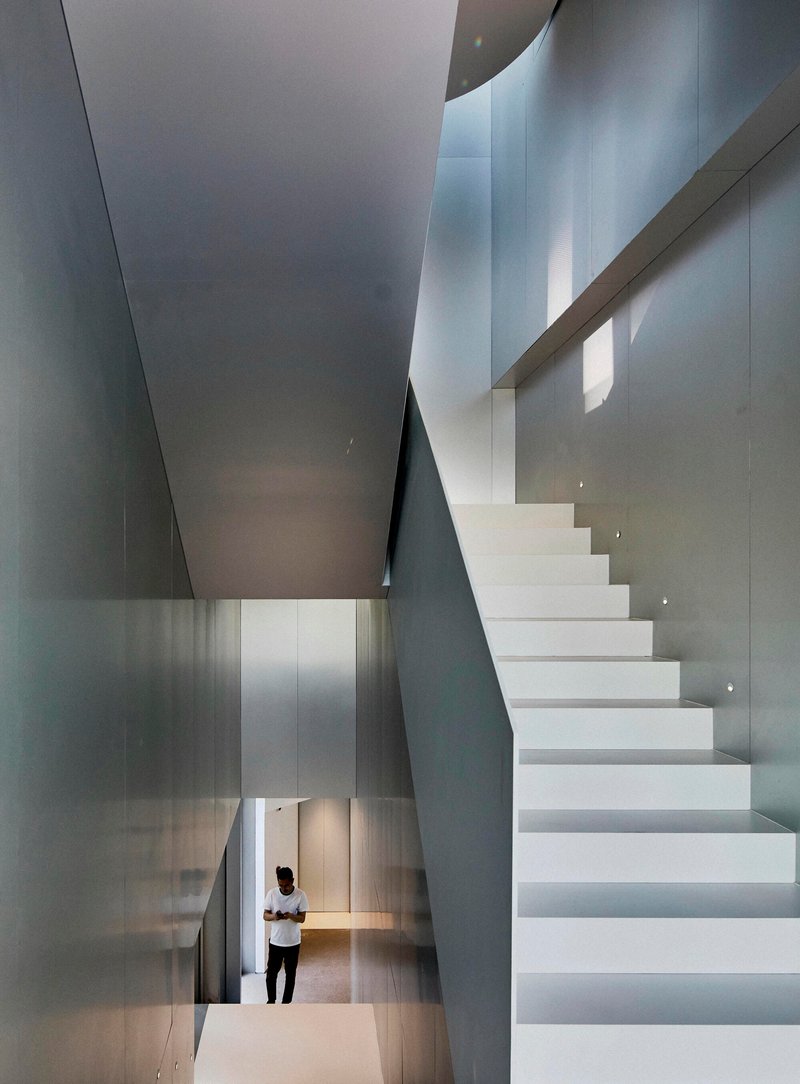 White cantilevered staircase rising through a multi-story volume with a figure visible below
