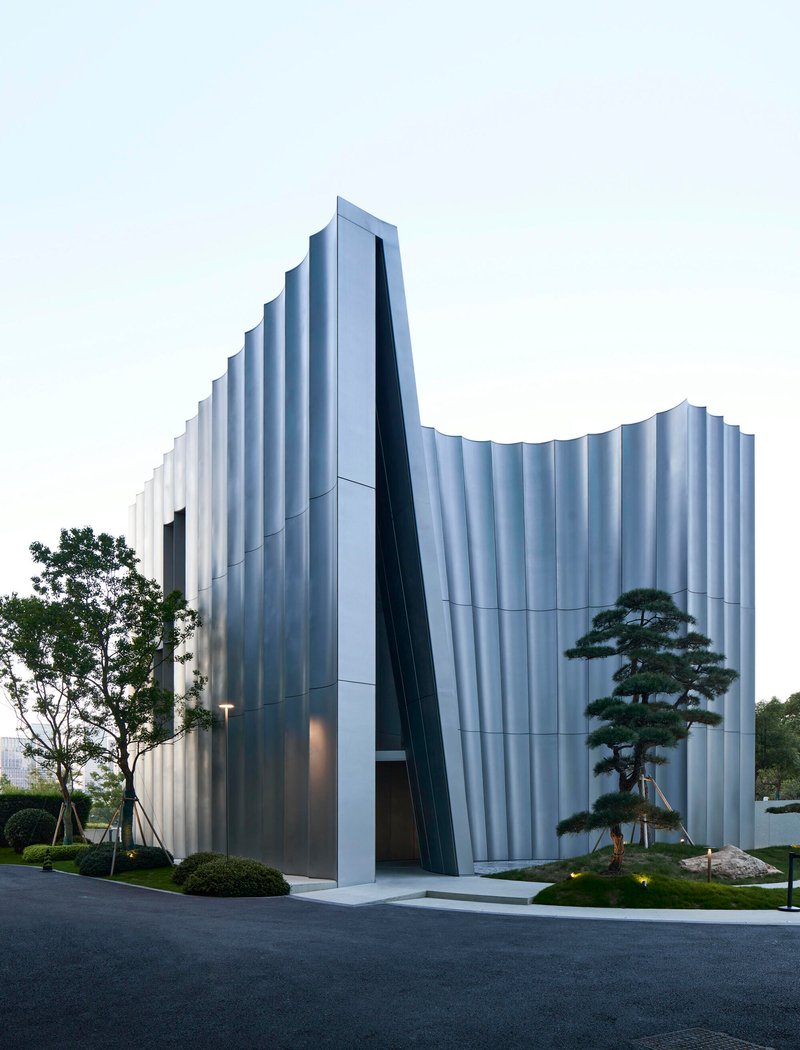 Street view of the undulating white facade with deep slanted entry void at dusk