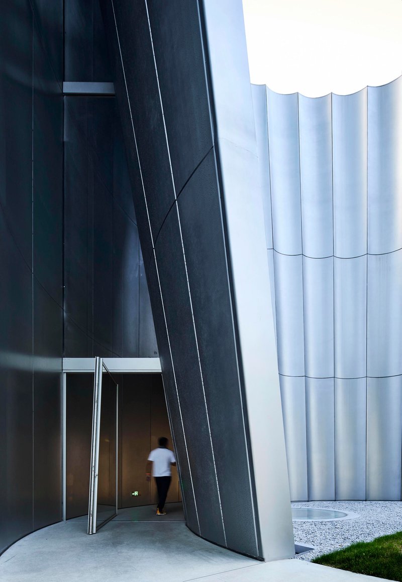 Entrance passage with dark angled wall and figure walking beneath the ribbed white exterior