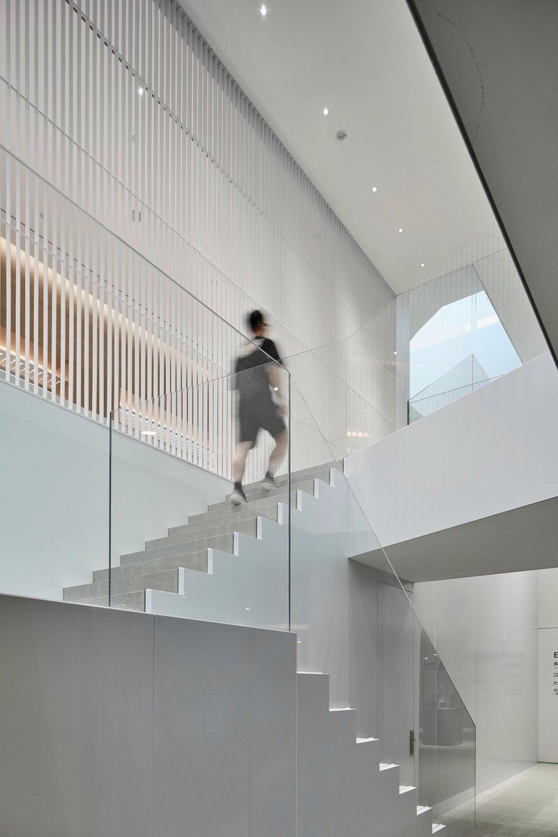 White cantilevered staircase with glass balustrade and vertical screen wall as figure descends