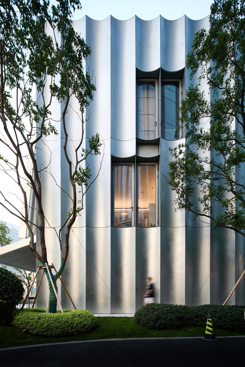Cylindrical tower with fluted white facade and recessed glazed openings framed by bare trees at dusk