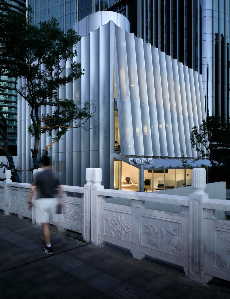 Fluted white volume with illuminated ground floor and pedestrian passing carved stone balustrade at dusk