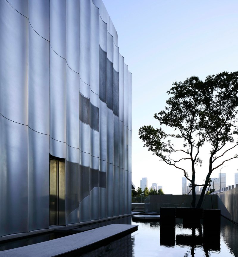 Close-up of white fluted facade with recessed glazing beside a silhouetted tree at twilight