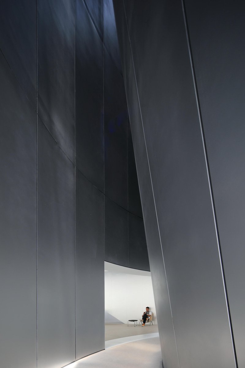 Narrow passage between towering dark panels leading to a seated figure in a lit room