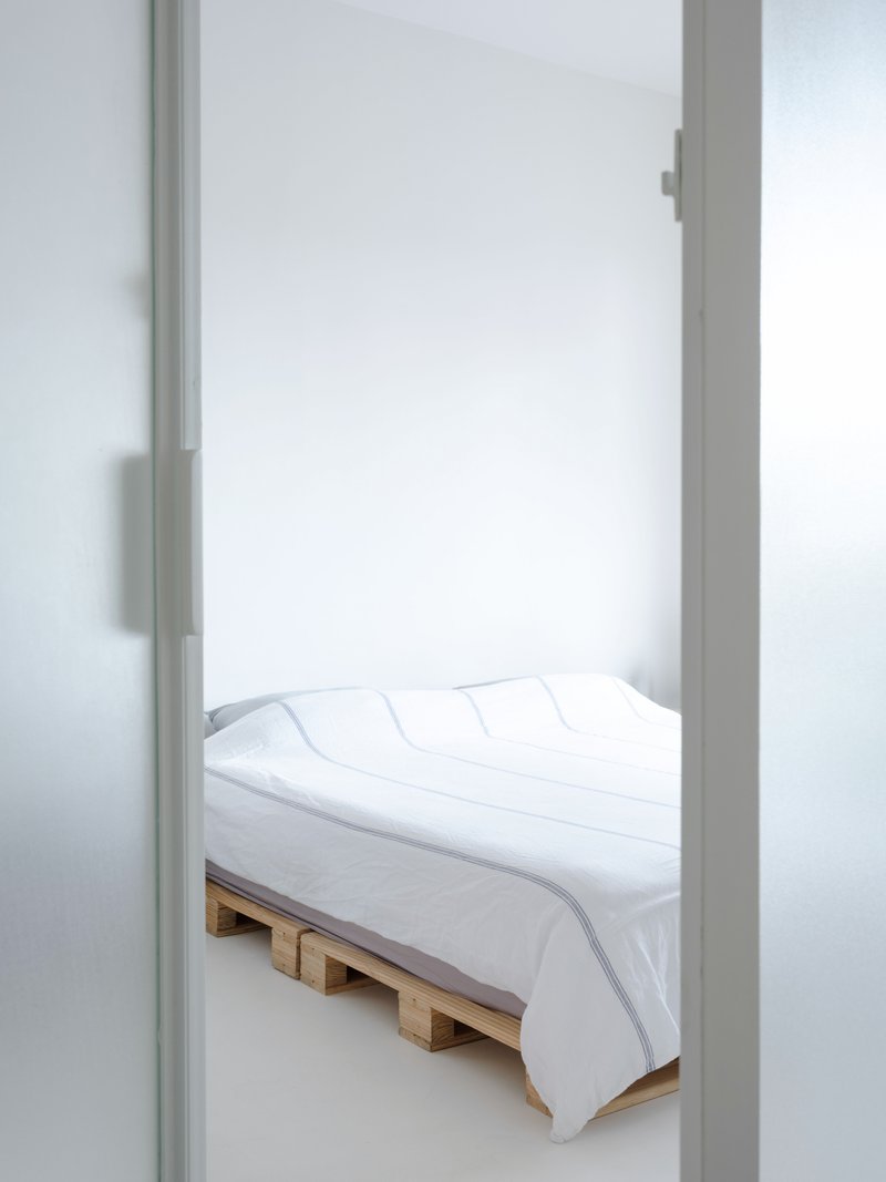View through frosted glass doorway into bedroom with timber pallet bed and white bedding
