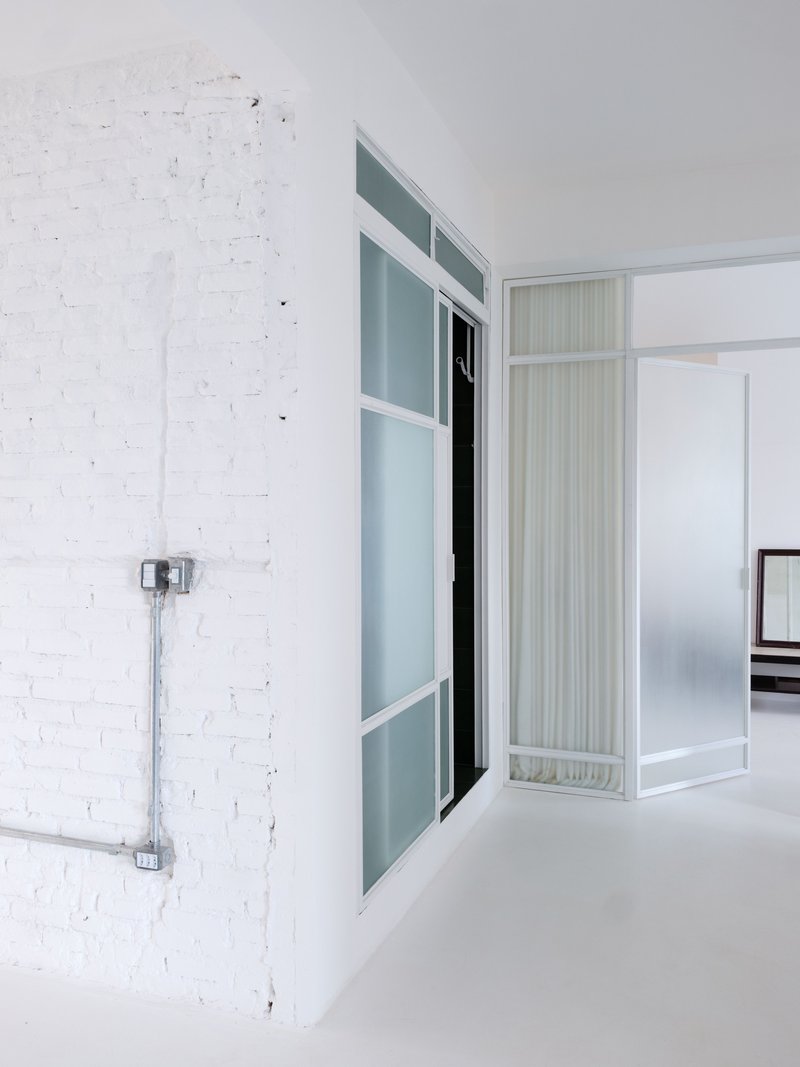 Interior partition with frosted glass panels and white frames against a painted brick wall with exposed conduit