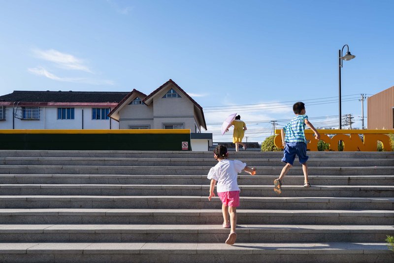 Wide concrete steps with children running up them beneath a blue sky and streetlamp
