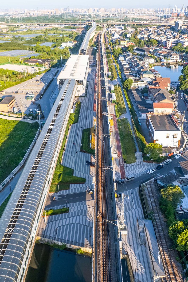 Aerial view of the curved glass-roofed train station with rail tracks cutting through residential neighborhoods