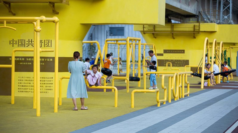 Yellow tubular playground structures with children and families playing beneath the concrete viaduct