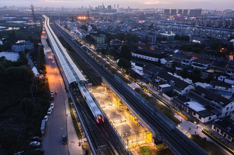 Aerial perspective of the illuminated platform canopy and yellow play areas along the tracks at dusk