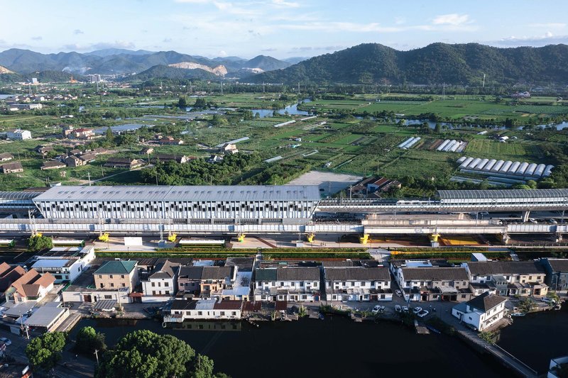 Aerial view of elevated station with tubular skylights spanning parallel rail tracks across agricultural landscape