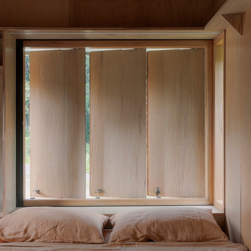 Bedroom window with three vertical timber panels framed in plywood above a linen-covered bed
