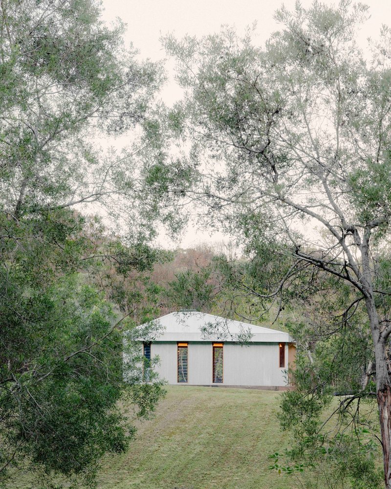 Rear view of the gabled volume in mist with twin openings visible through surrounding eucalyptus trees