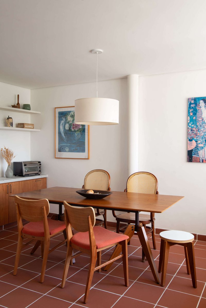Dining area with wooden table and cane-backed chairs on terracotta tile floor under pendant light