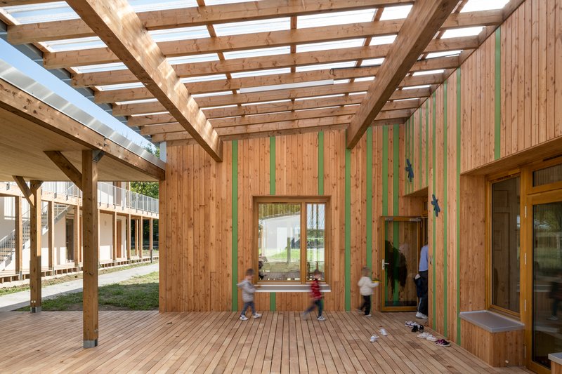 Courtyard view of timber cladding with green vertical stripes and children playing under the pergola