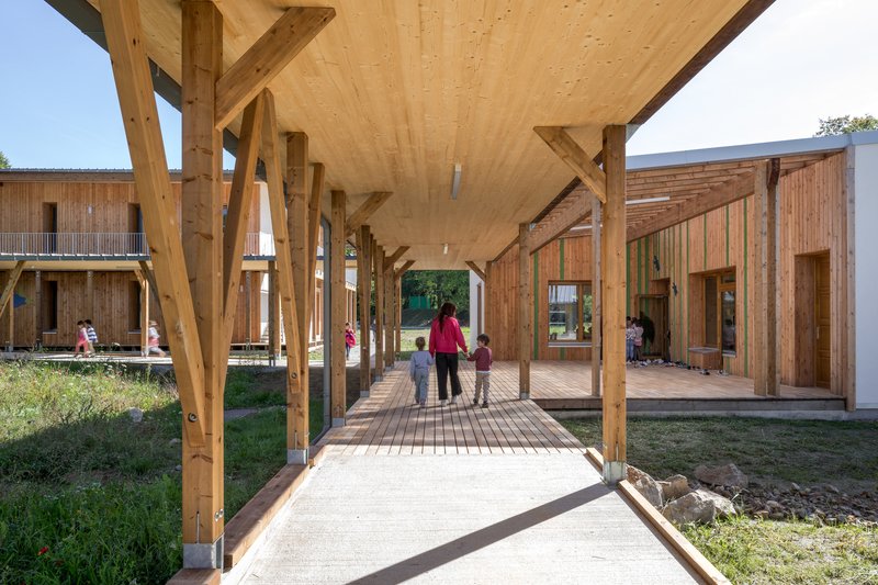 Covered walkway with laminated timber columns and plywood ceiling as a caregiver walks with children