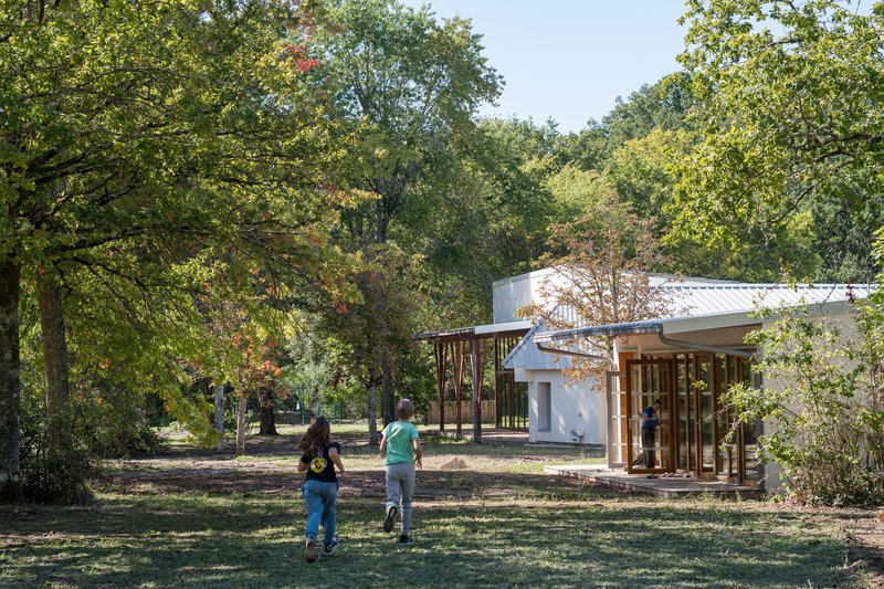 White gabled pavilion with timber columns viewed through trees as two children run across the lawn
