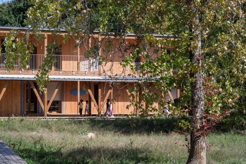 Two-level timber facade with diagonal bracing and upper balcony seen through foreground trees
